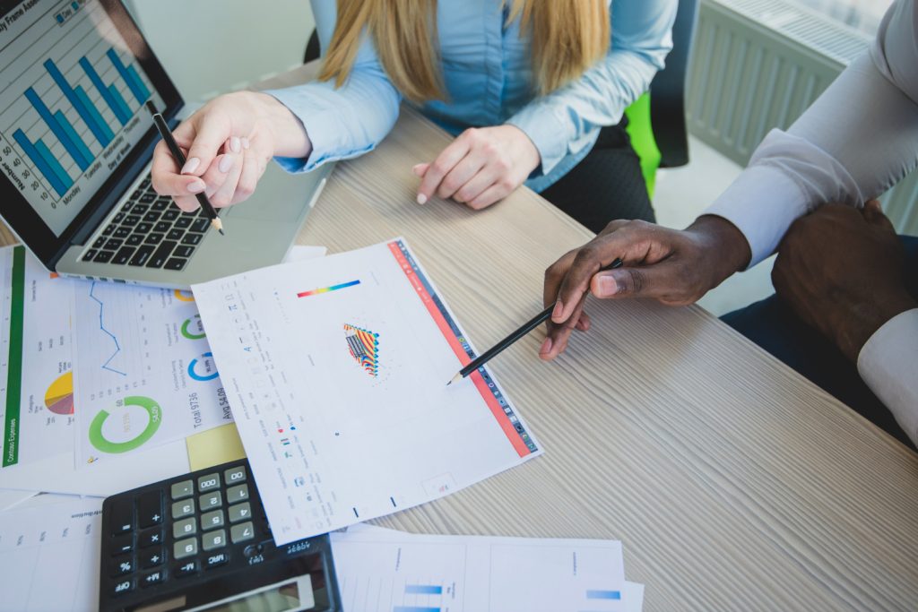 wo professionals analyzing financial charts and graphs at a desk, with a laptop, calculator, and printed documents spread out, discussing data insights and business strategies.