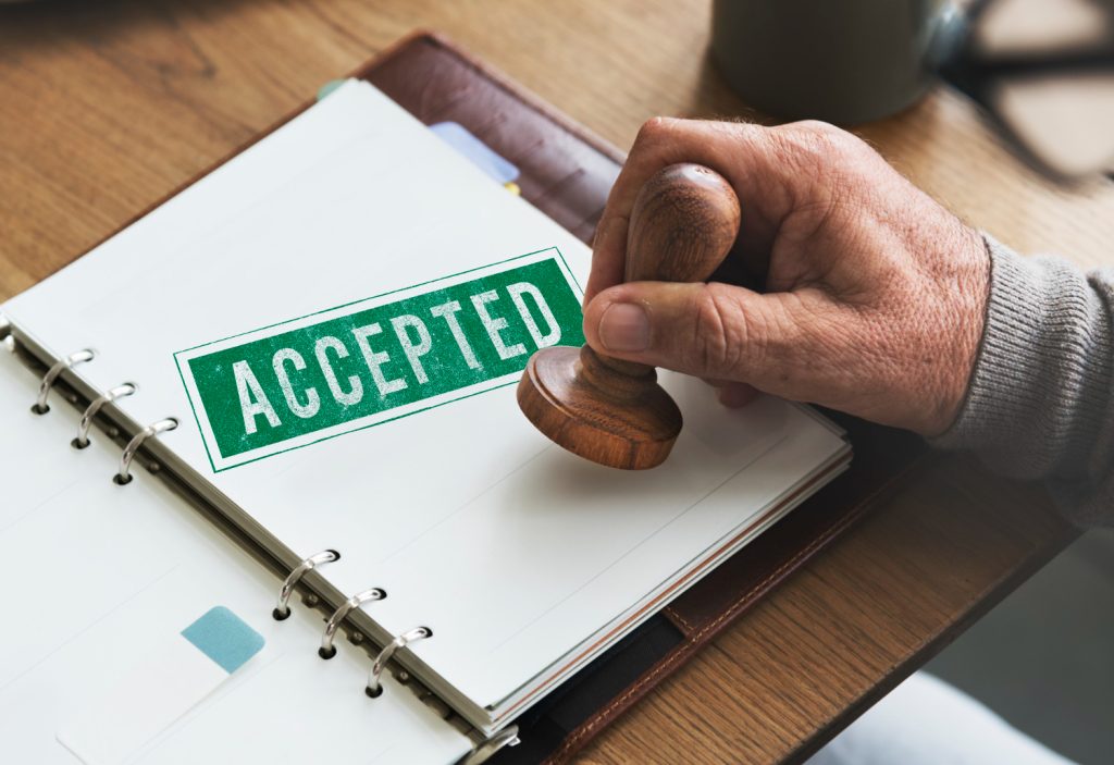 A hand stamping a document with a green 'ACCEPTED' mark in an open binder, symbolizing financing approval or acceptance.